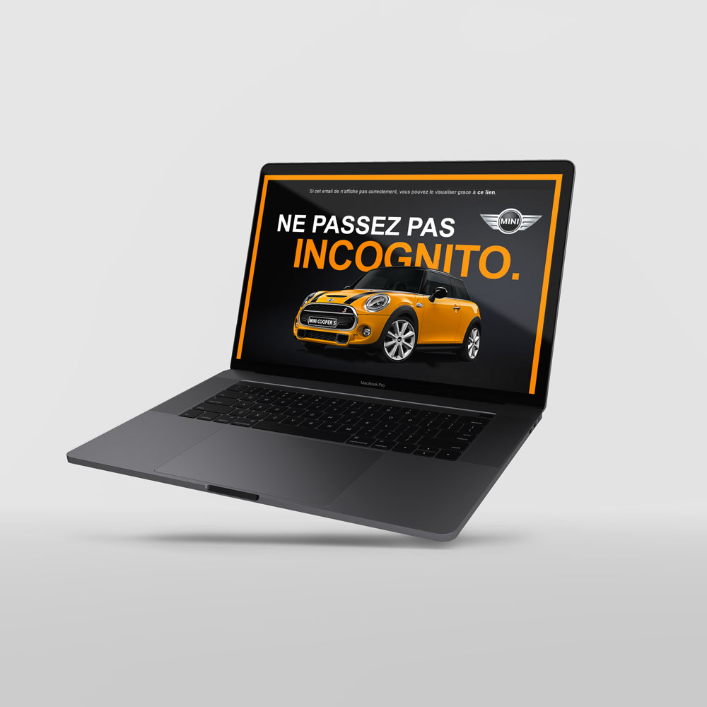 MacBook Pro gris anthracite de 3/4 sur fond gris clair, avec visuel d'une newsletter MINI présentant la nouvelle 3 porte de couleur orange/jaune